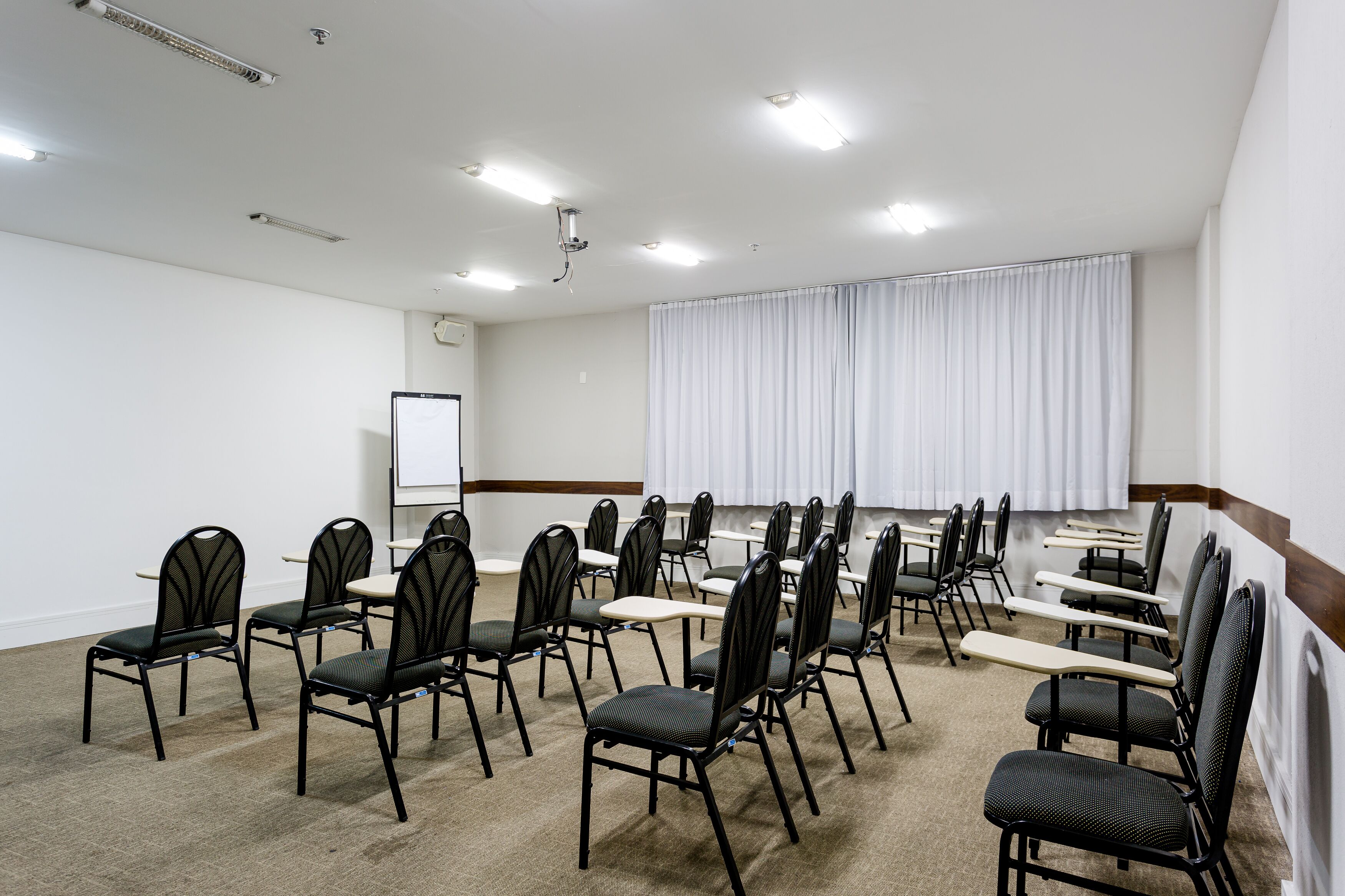 A conference room with rows of chairs, a whiteboard, and a large window with curtains.
