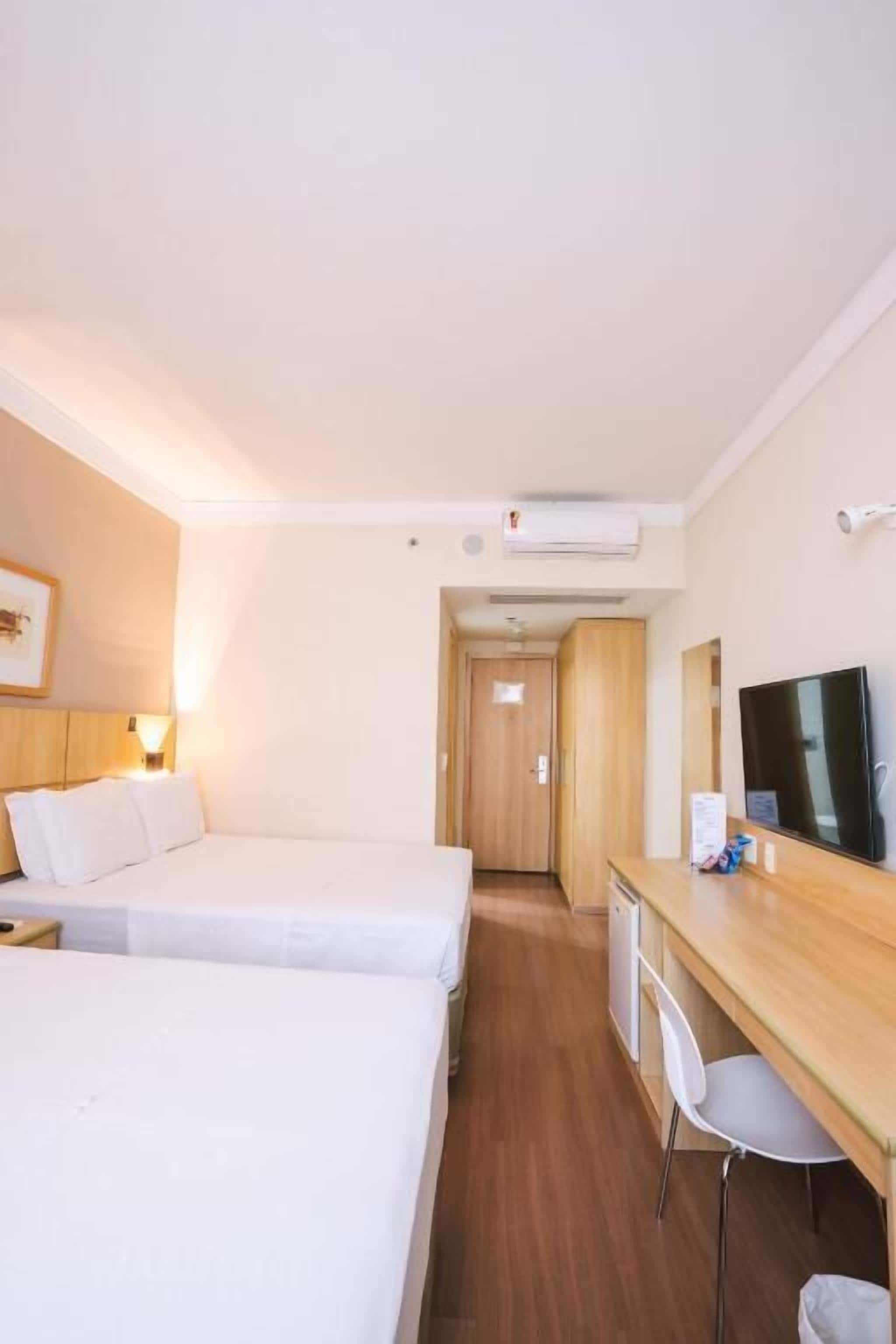 Una camera d'albergo con due letti, una scrivania, una sedia, un televisore e un condizionatore.