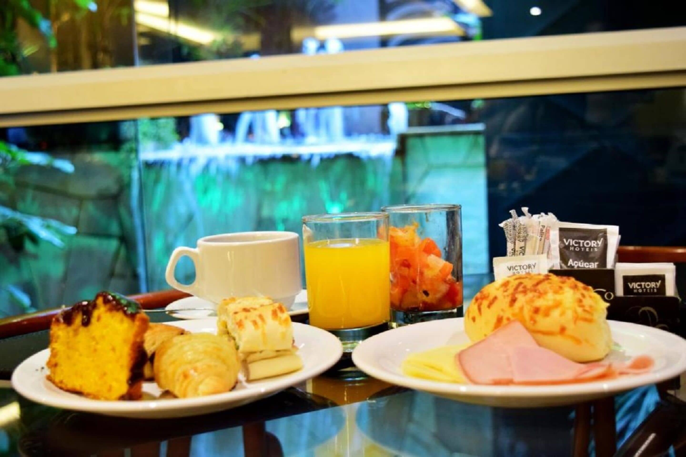 A breakfast table with croissants, a slice of cake, a glass of orange juice, and a plate with ham and cheese.