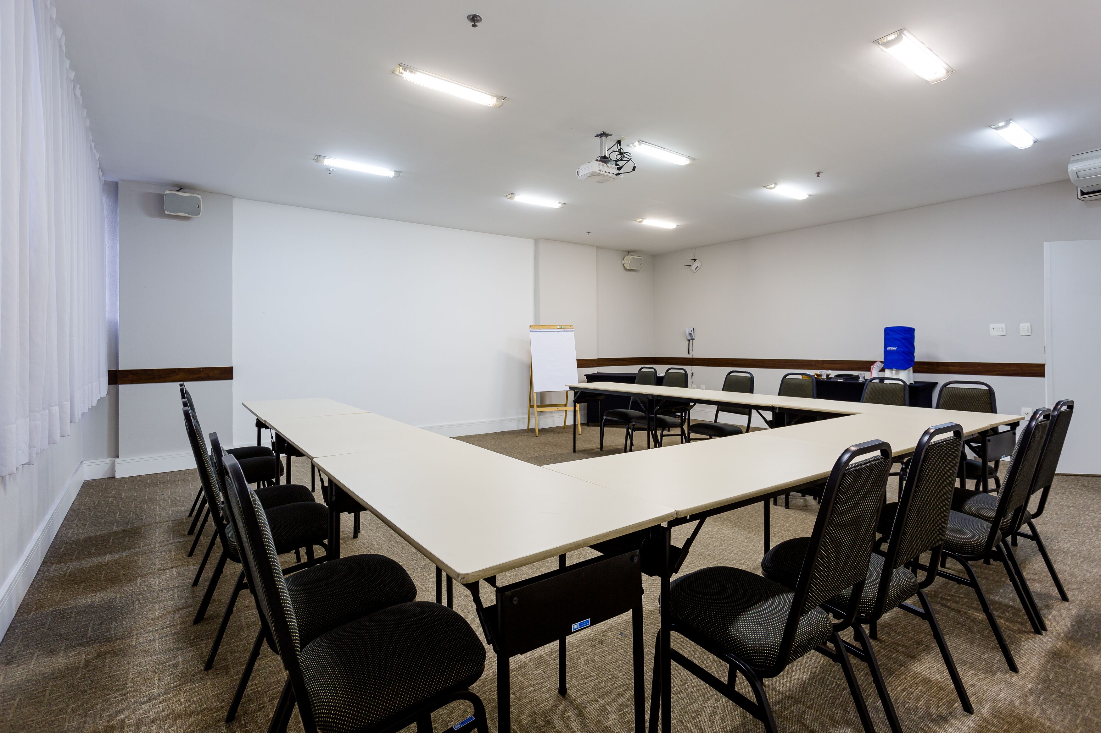 Un salón de conferencias con una larga mesa, sillas, una pizarra y un proyector.