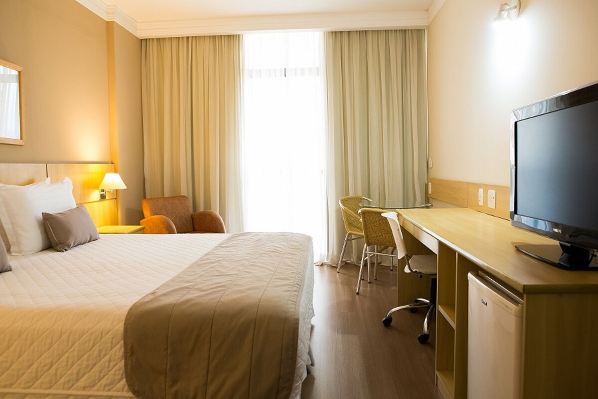 A hotel room with a bed, desk, chair, television, and curtains.