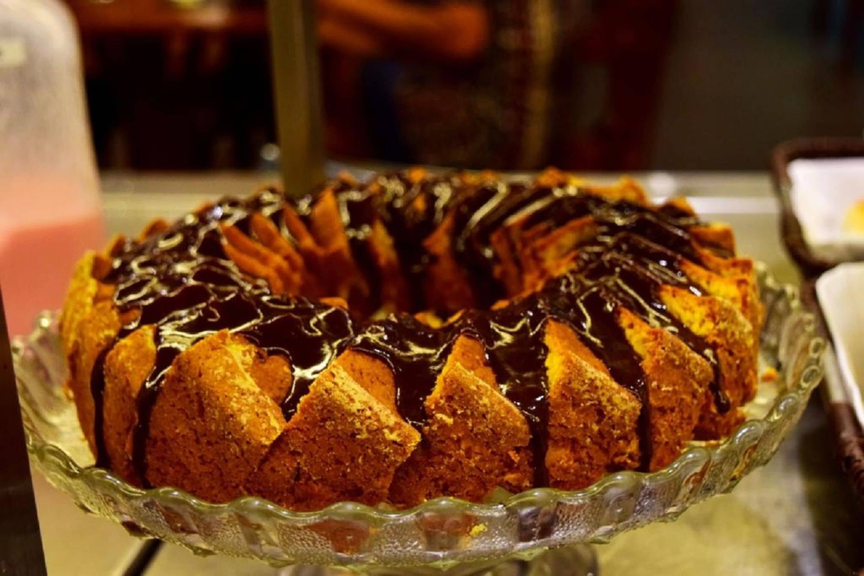 Un pastel Bundt con glaseado de chocolate sobre un pedestal de vidrio.
