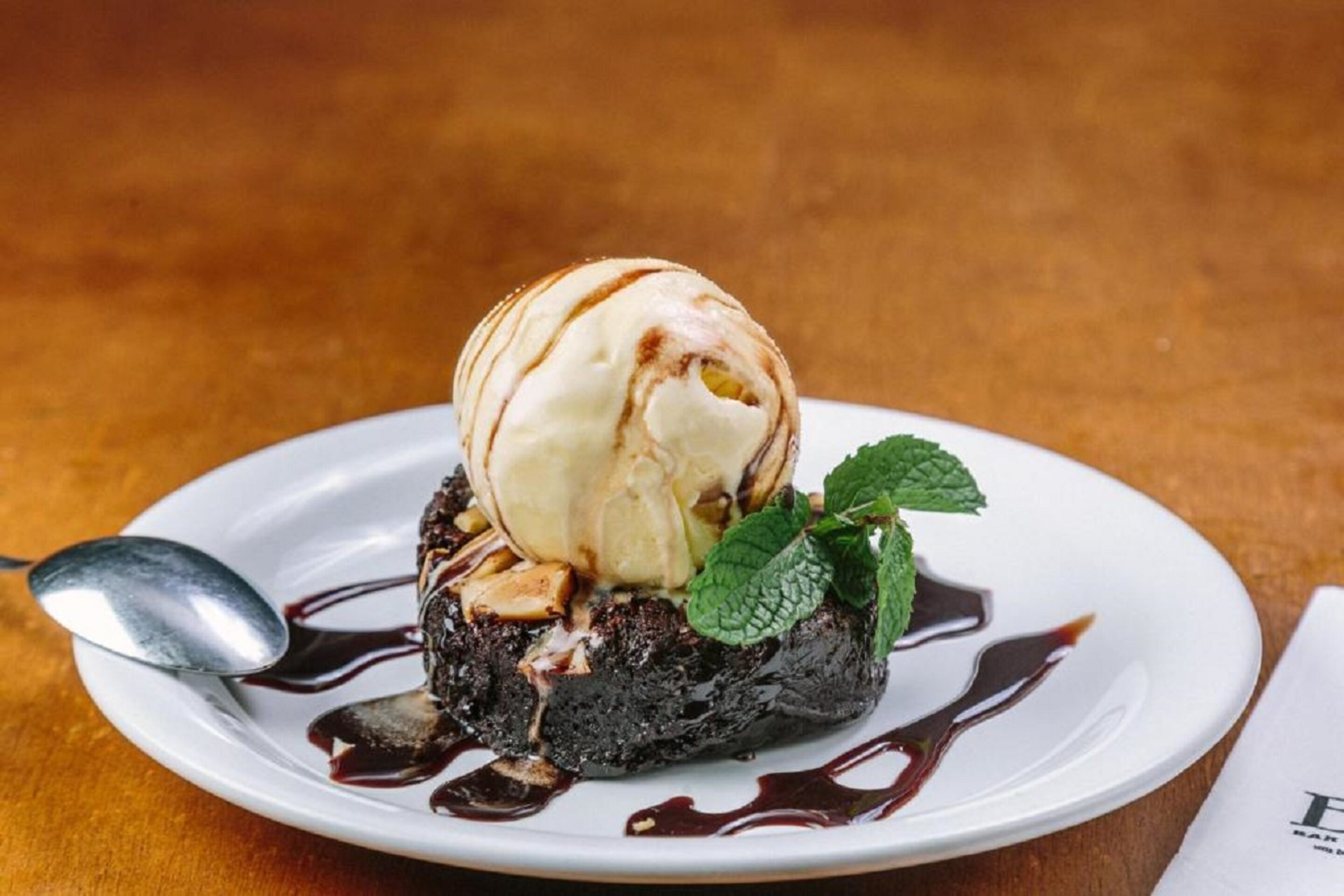 Un postre en un plato blanco, con una cuchara y adornado con hojas de menta.