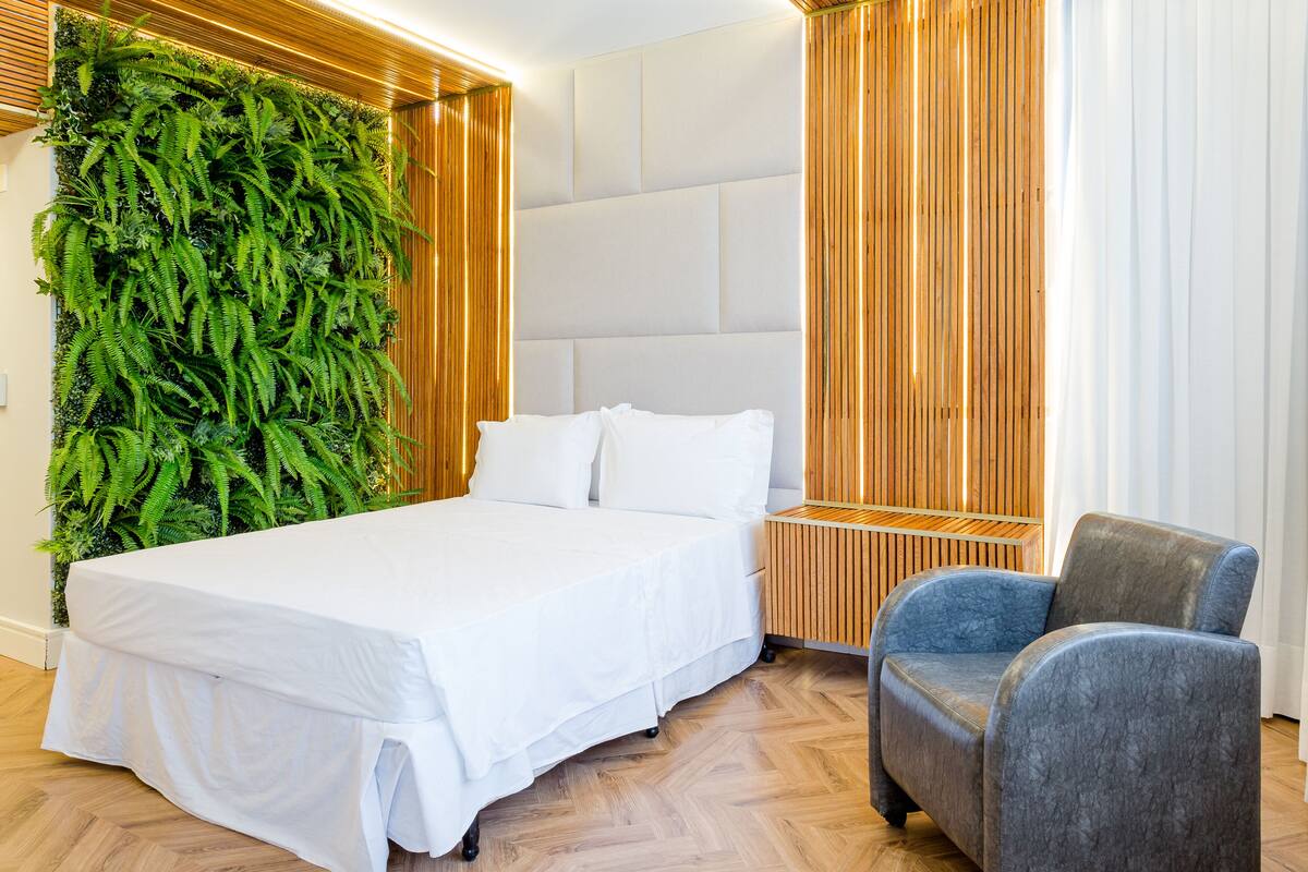 Ein modernes Hotelzimmer mit einem großen Bett, einem blauen Sessel, einer vertikalen Grünwand und Holzverkleidung.