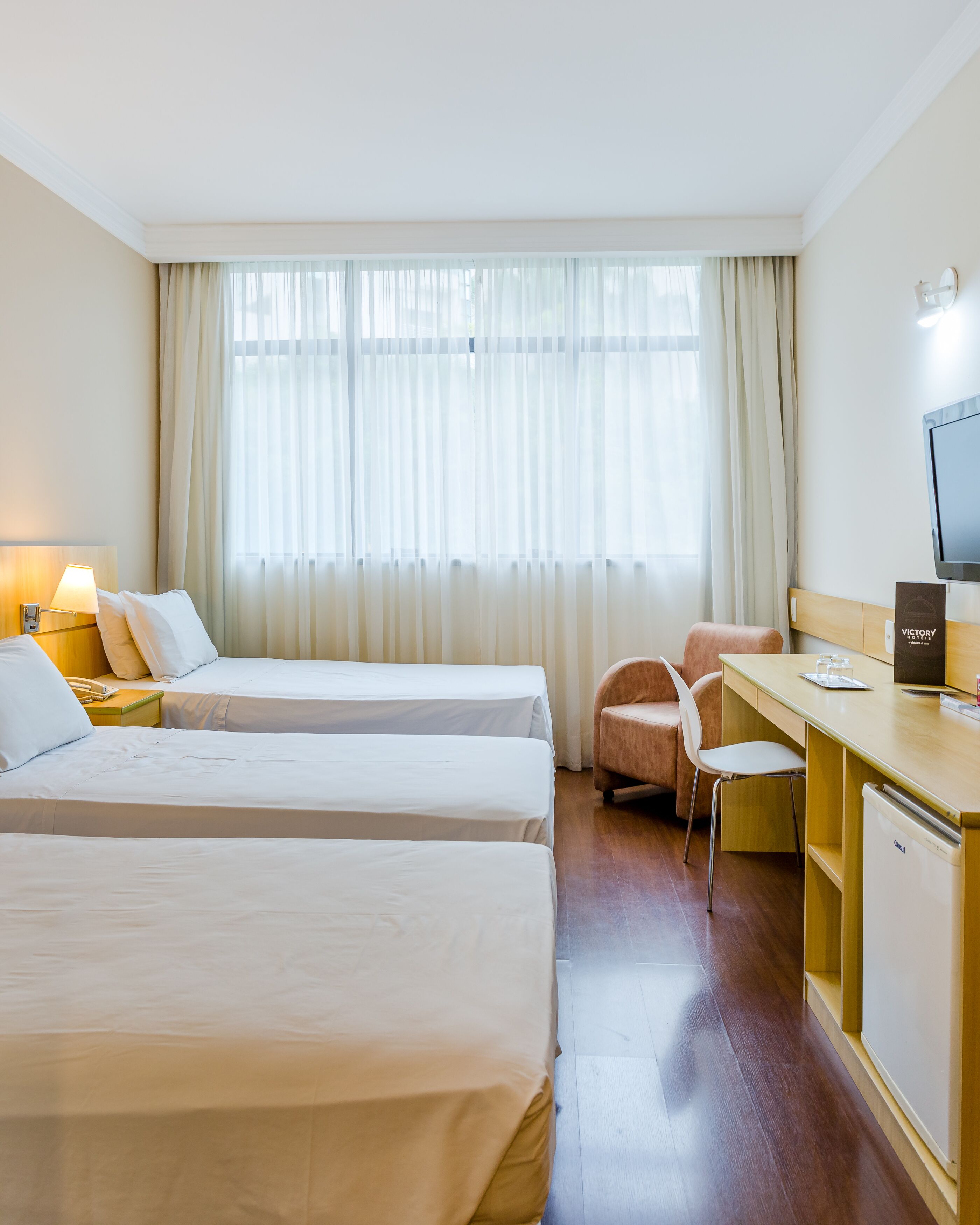 Habitación de hotel con dos camas, un escritorio, una silla, un televisor y un minibar.