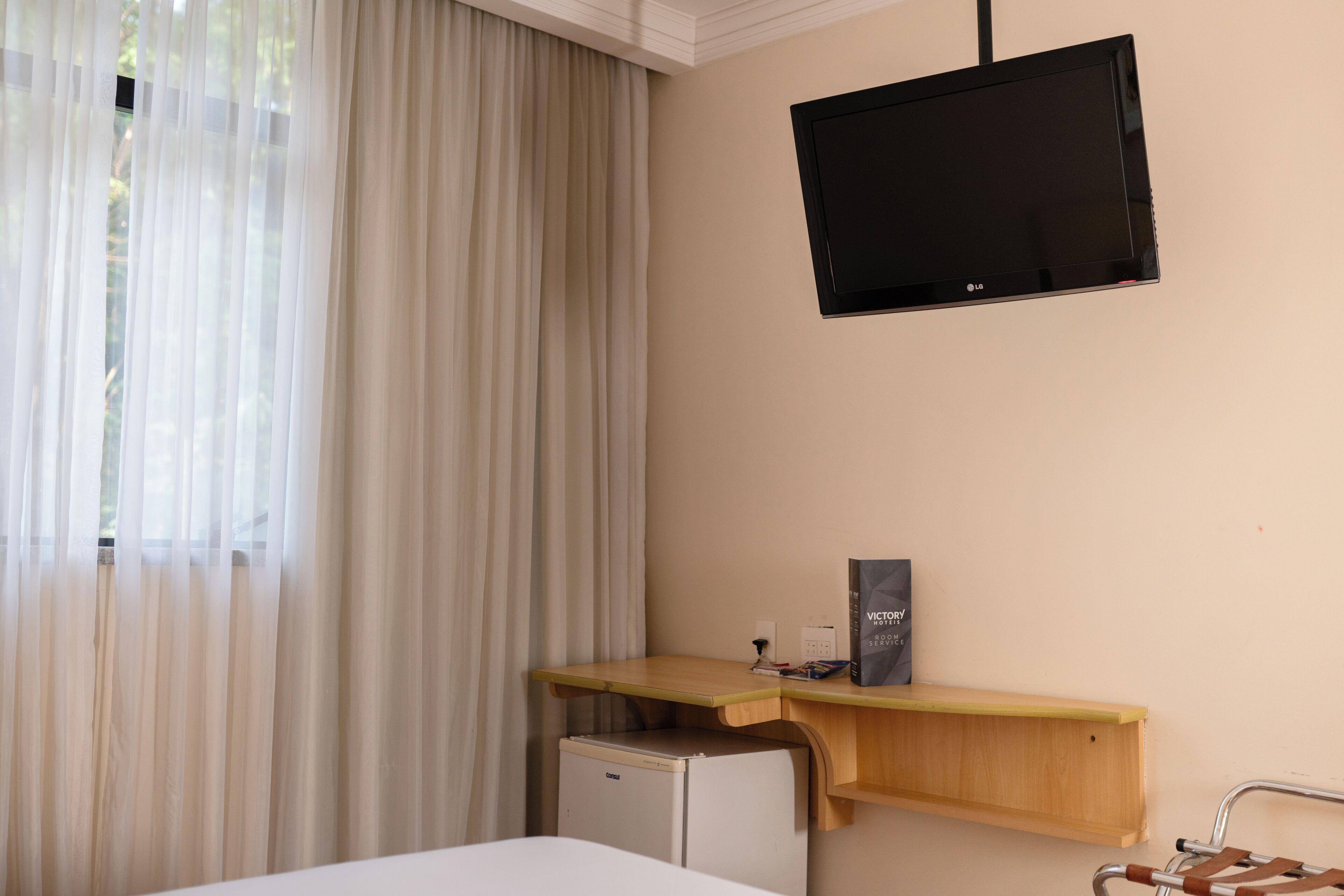 A hotel room with a bed, a desk with a computer, a television, and a small refrigerator.