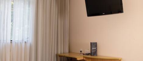 A hotel room with a bed, a desk with a computer, a television, and a small refrigerator.