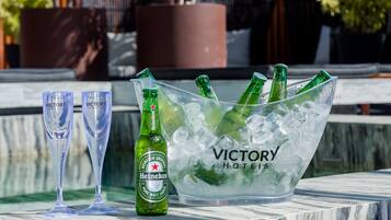 Un cubo de hielo transparente con botellas de cerveza Heineken y vasos sobre una superficie de mármol.