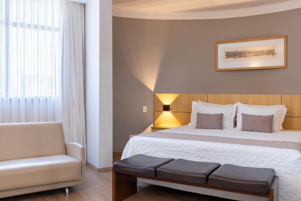 Una habitación de hotel con cama, un banco, un sofá y una lámpara.