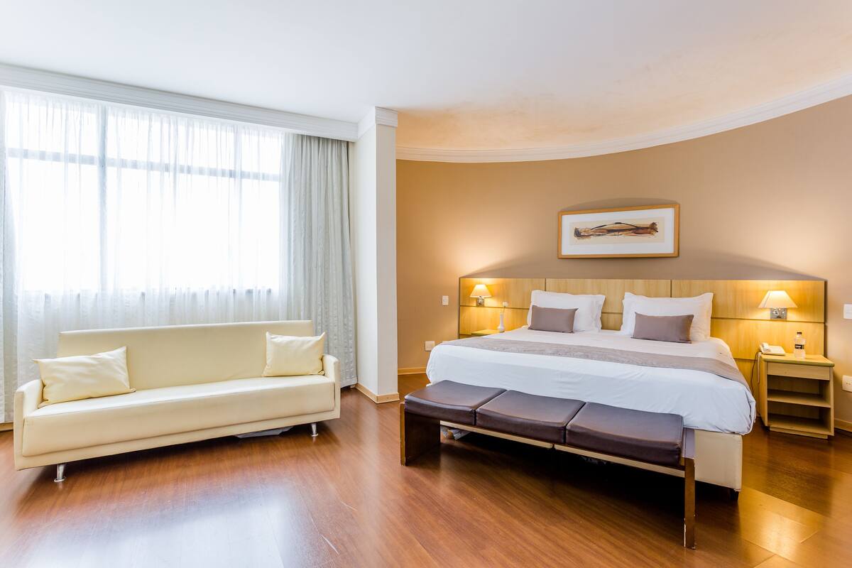 Ein Hotelzimmer mit Bett, Nachttischen, einer Couch und einem großen Fenster mit Vorhängen.