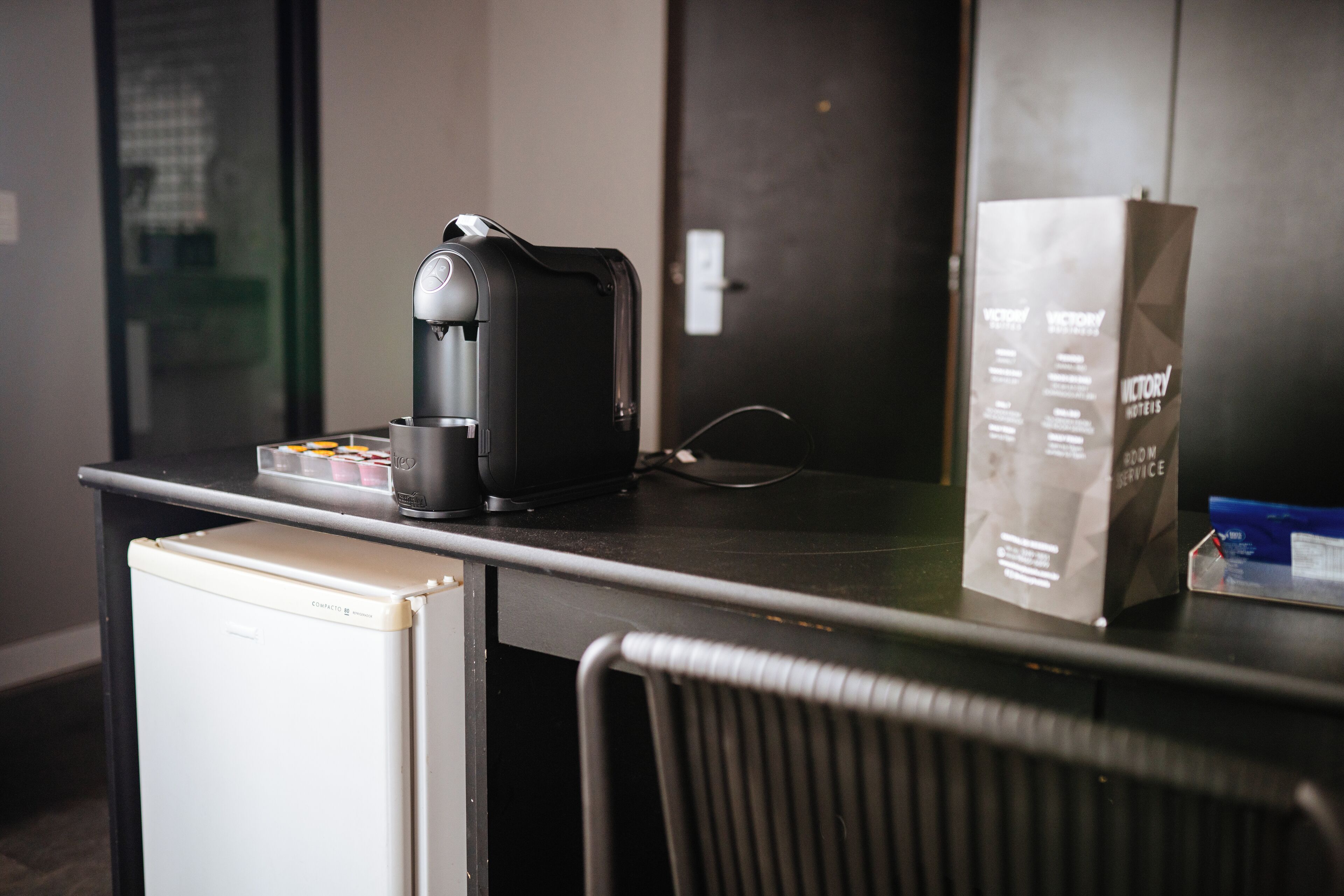 A small kitchenette with a coffee maker, a refrigerator, and a bag of toiletries on a counter.