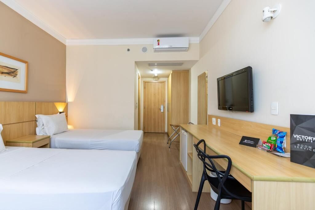 Habitación de hotel con dos camas, un escritorio con silla, televisión y un cuadro en la pared.