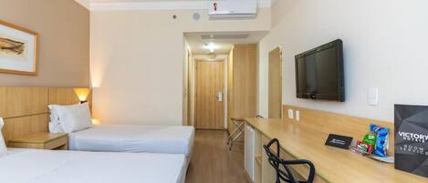 Habitación de hotel con dos camas, un escritorio con silla, televisión y un cuadro en la pared.