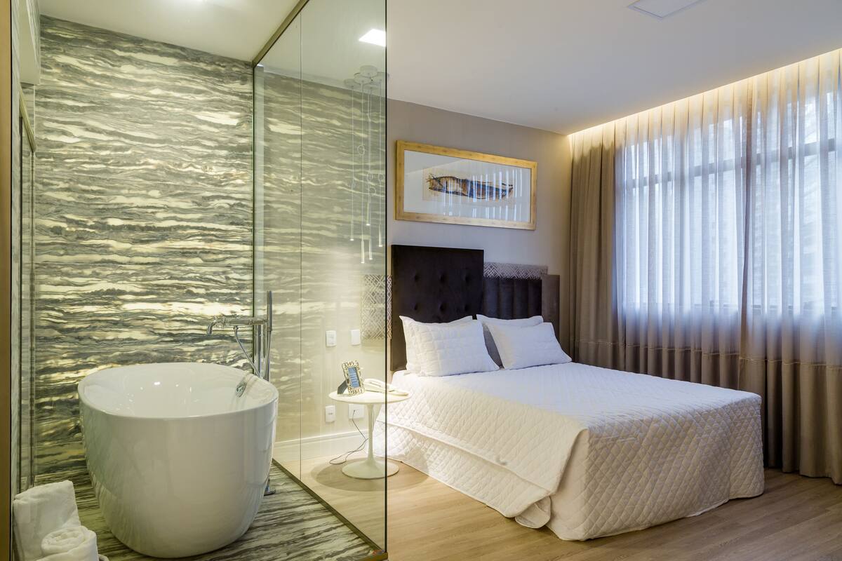 Ein modernes Hotelzimmer mit einer großen Badewanne, einem ordentlich bezogenen Bett und einer gläsernen Duschkabine.