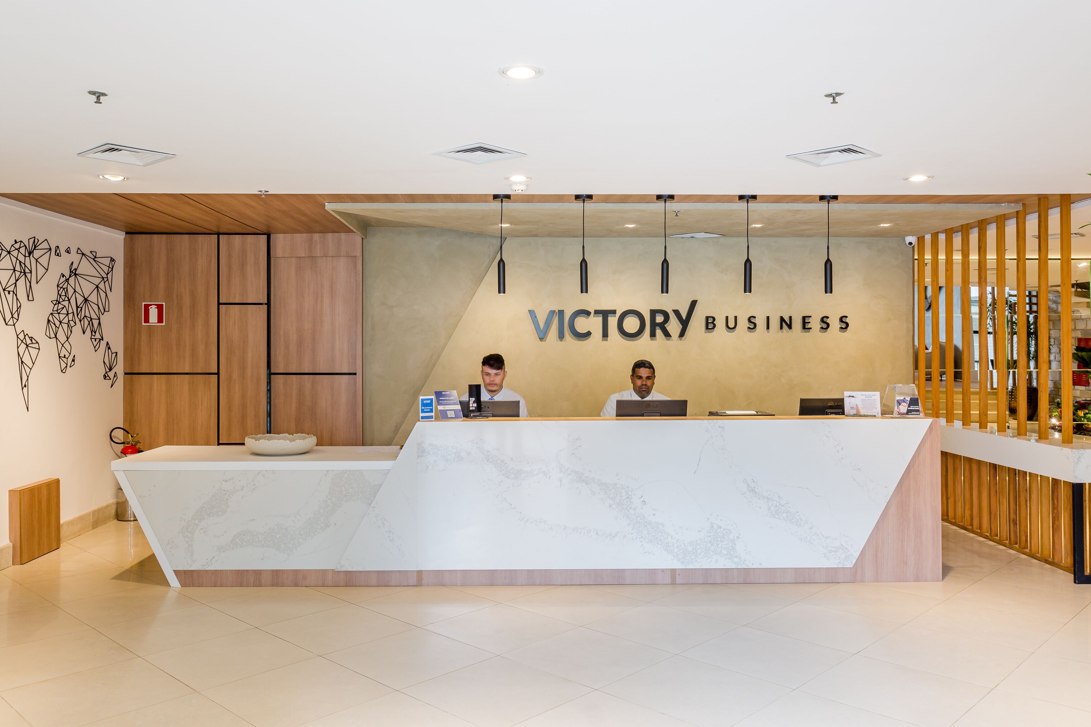 Un mostrador de recepción con encimera de mármol, dos empleados detrás y una pared con el letrero "VICTORY BUSINESS". 