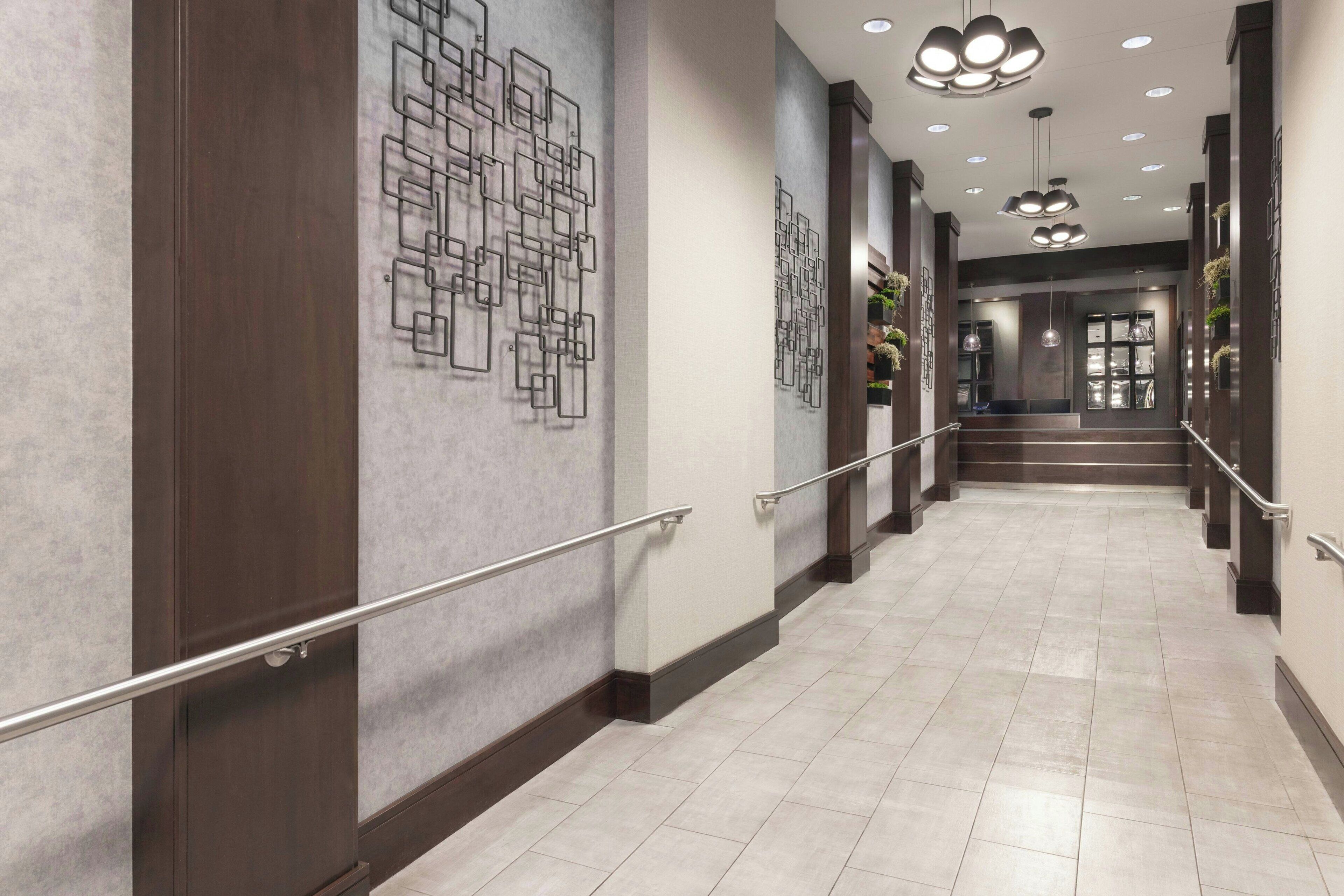 A modern hotel corridor with a tiled floor, wooden paneling, and a metal handrail.
