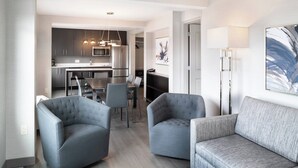 Un salon moderne avec des canapés gris, un coin repas et une cuisine équipée d’appareils électroménagers en acier inoxydable.