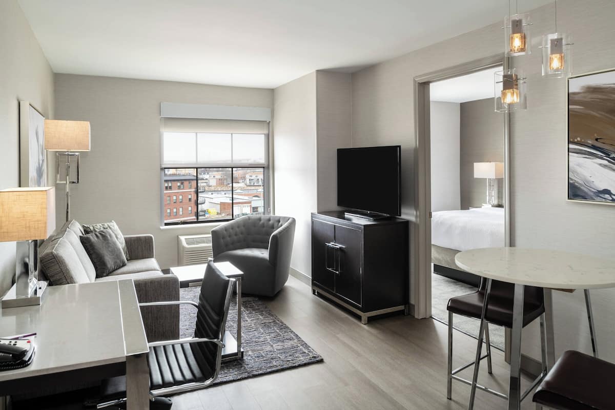 Ein modernes Hotelzimmer mit Flachbildfernseher, Esstisch, Sofa und Sessel.