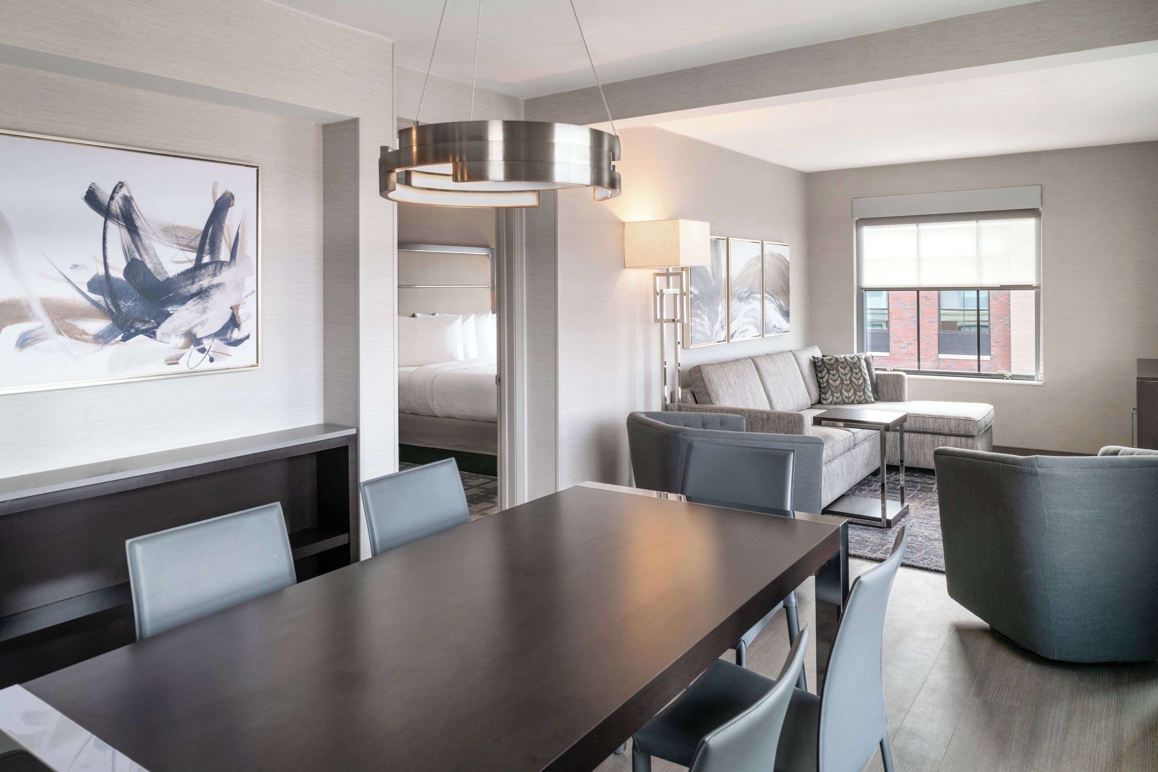A modern hotel room with a dining area, a sofa set, and a large window.