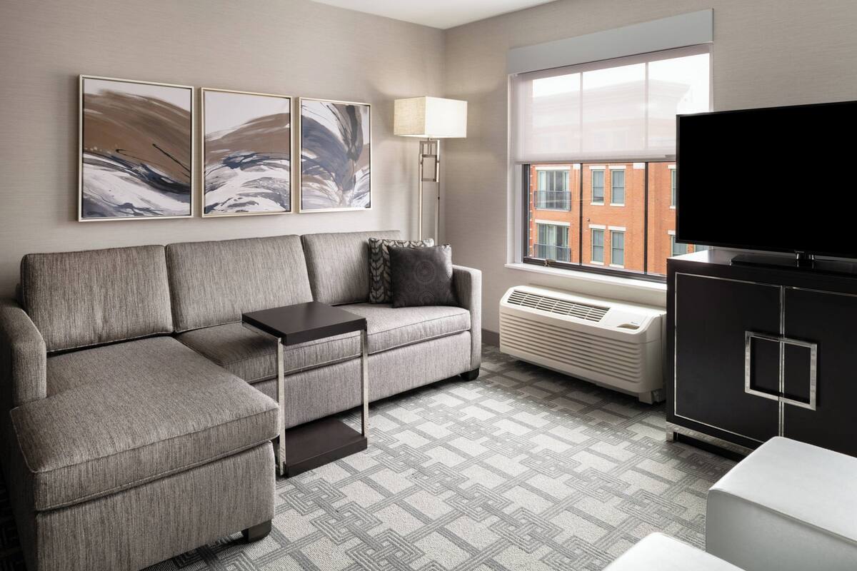 Ein modernes Wohnzimmer mit einem Ecksofa, einem Flachbildfernseher, einer Stehlampe und Kunstwerken an der Wand.