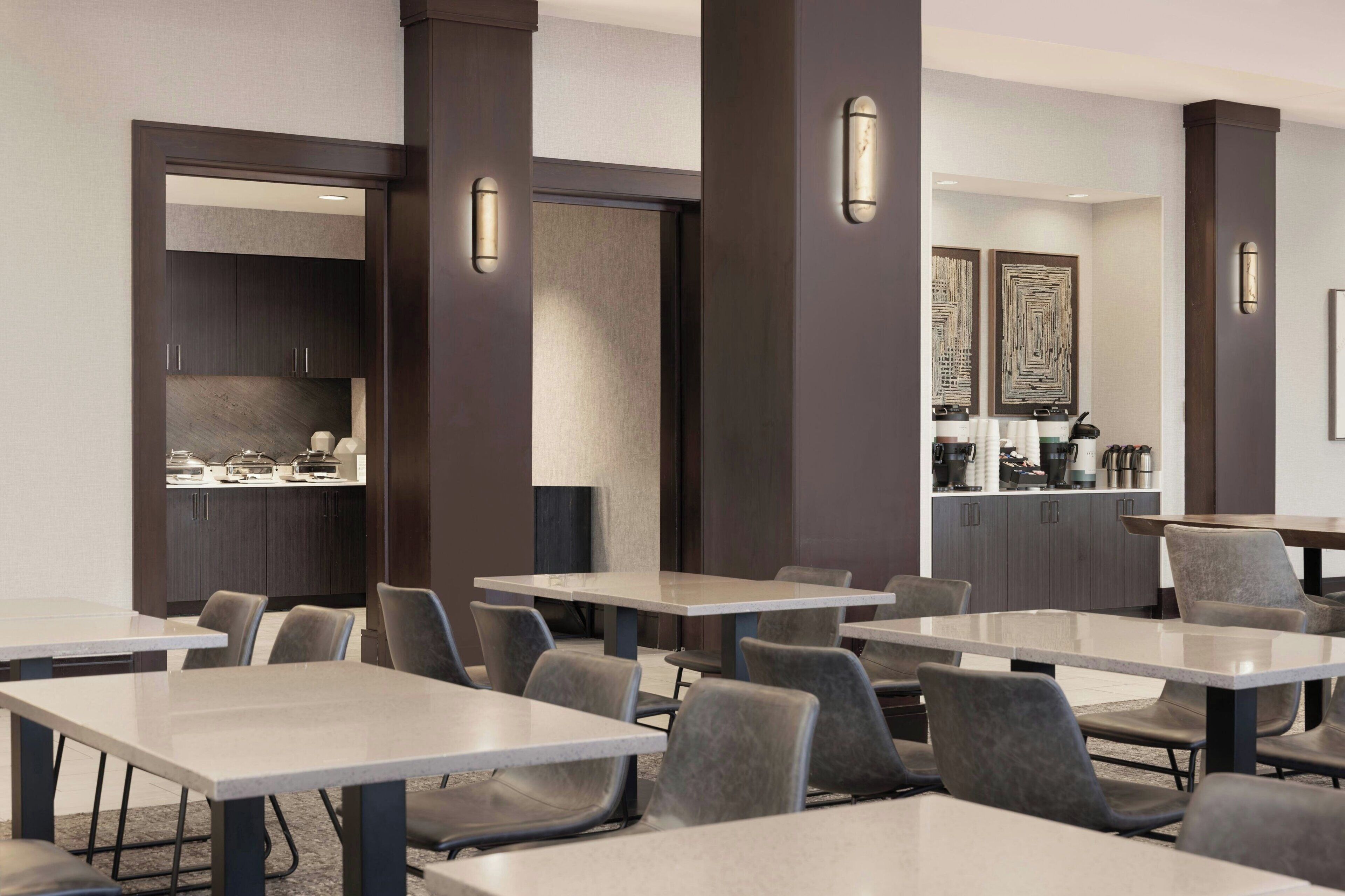 Une salle de réunion moderne, dotée de plusieurs tables et chaises, d’un coin cuisine et d’œuvres d’art décoratives sur les murs.