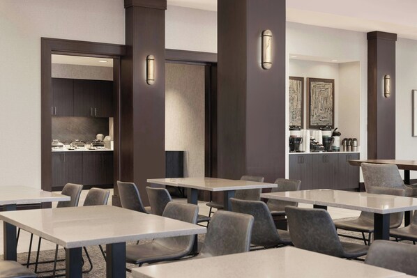 A modern meeting room with multiple tables and chairs, a kitchenette, and decorative wall art.
