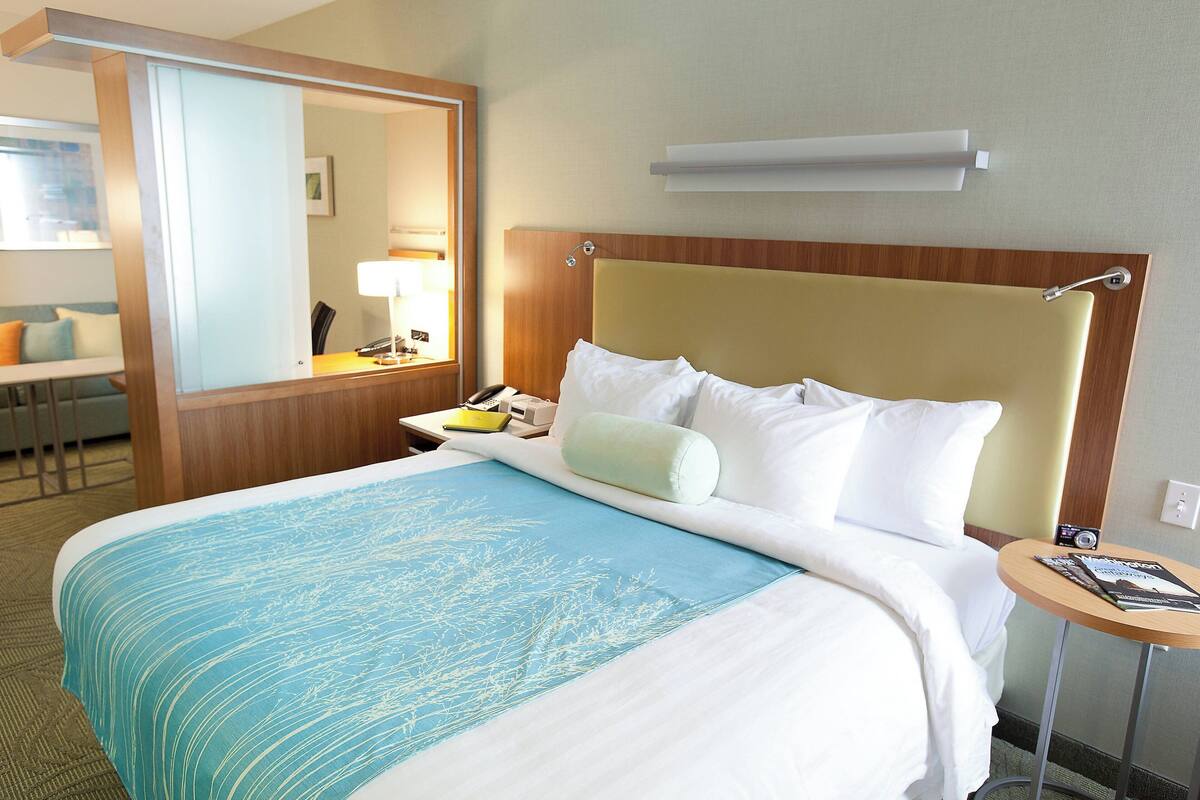 A hotel room with a bed, a bedside table, a chair, a desk, and a mirror.