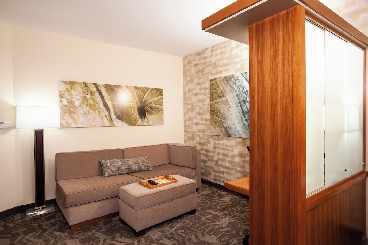 A modern hotel room with a beige sofa, a wooden side table, and two abstract paintings on the wall.