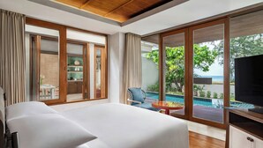 A modern hotel room with a large bed, a TV, and a view of a pool and beach.