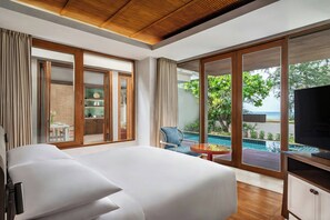 A modern hotel room with a large bed, a TV, and a view of a pool and beach.