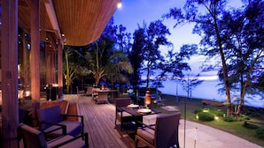 An outdoor deck with wooden furniture, a table set for dining, and a view of the ocean at dusk. - Renaissance Phuket Resort & Spa (Mai Khao)