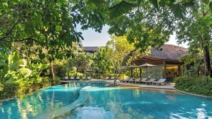 A swimming pool surrounded by lush greenery, with lounge chairs and umbrellas.