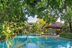 A swimming pool surrounded by lush greenery, with lounge chairs and umbrellas.