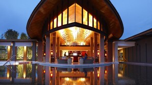 A modern building with a curved roof, a pool reflecting the structure, and a well-lit interior. - Renaissance Phuket Resort & Spa (Mai Khao)