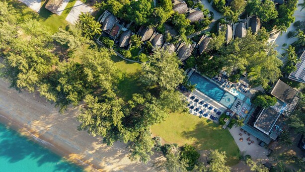 An aerial view of a resort with a swimming pool, beach, and lush greenery.