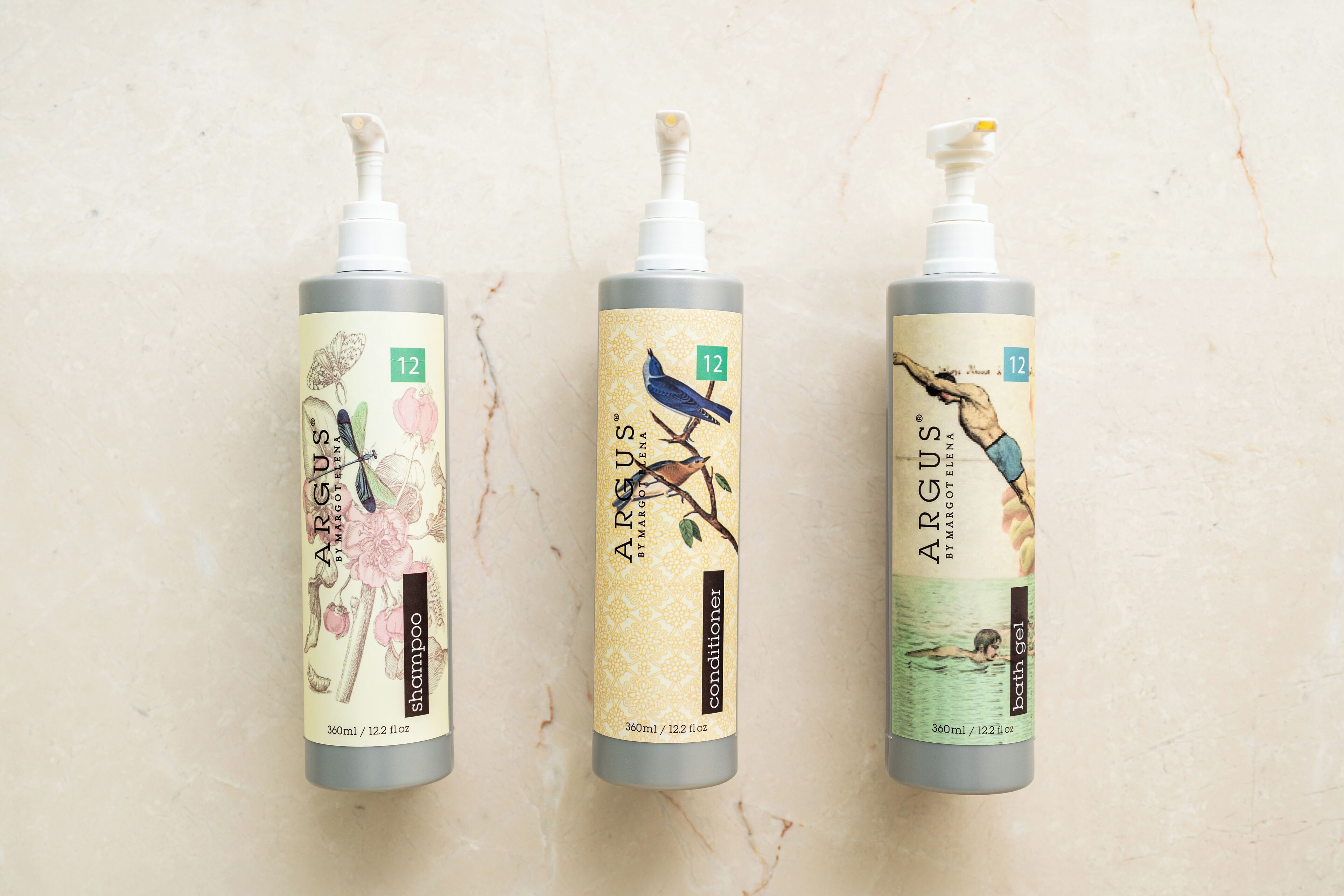 Três embalagens de produtos Argus por Margaret E. Ellis: shampoo, condicionador e gel de banho, cada um com uma ilustração exclusiva e rotulado com o número 12.