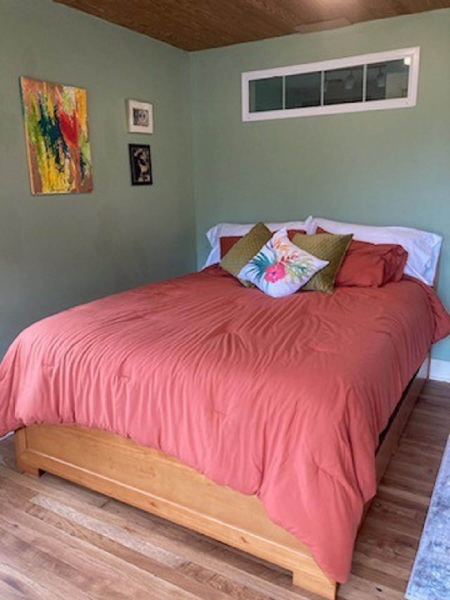 A bedroom with a wooden bed frame, a pink bedspread, and a window above the bed.