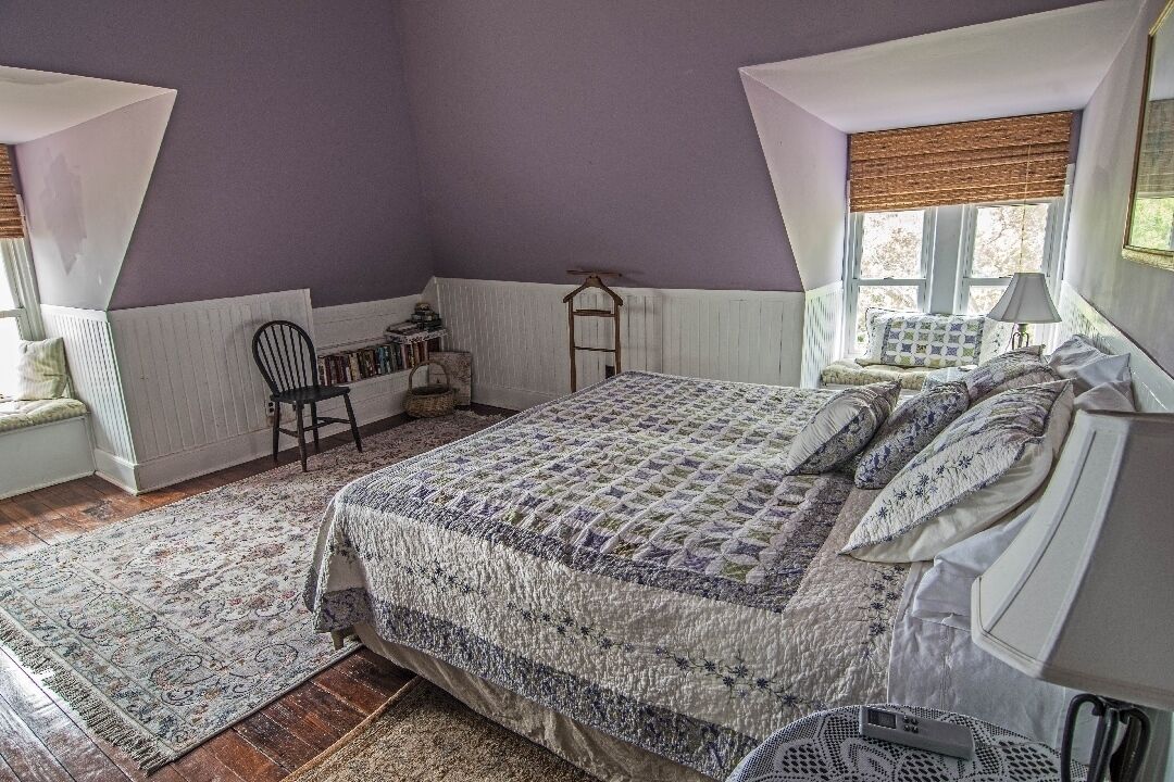 A bedroom with a large bed, a chair, a small table, and a window with a view.