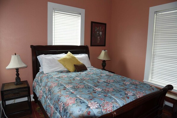 A bedroom with a floral bedspread, two bedside lamps, a nightstand, and a window with blinds.