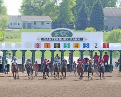 Una carrera de caballos en Canterbury Park, con barreras numeradas y jinetes a caballo.