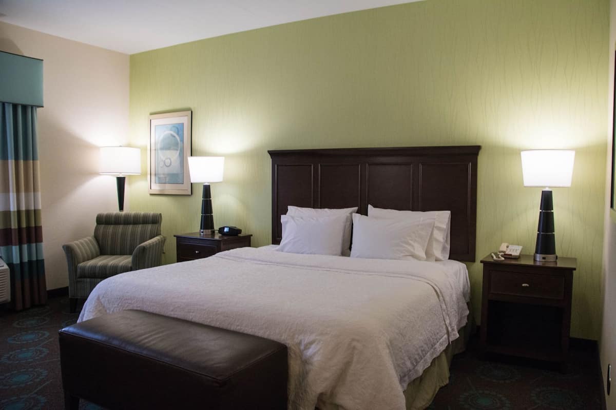 A hotel room with a large bed, two bedside tables, a chair, a bench, and a framed picture on the wall.