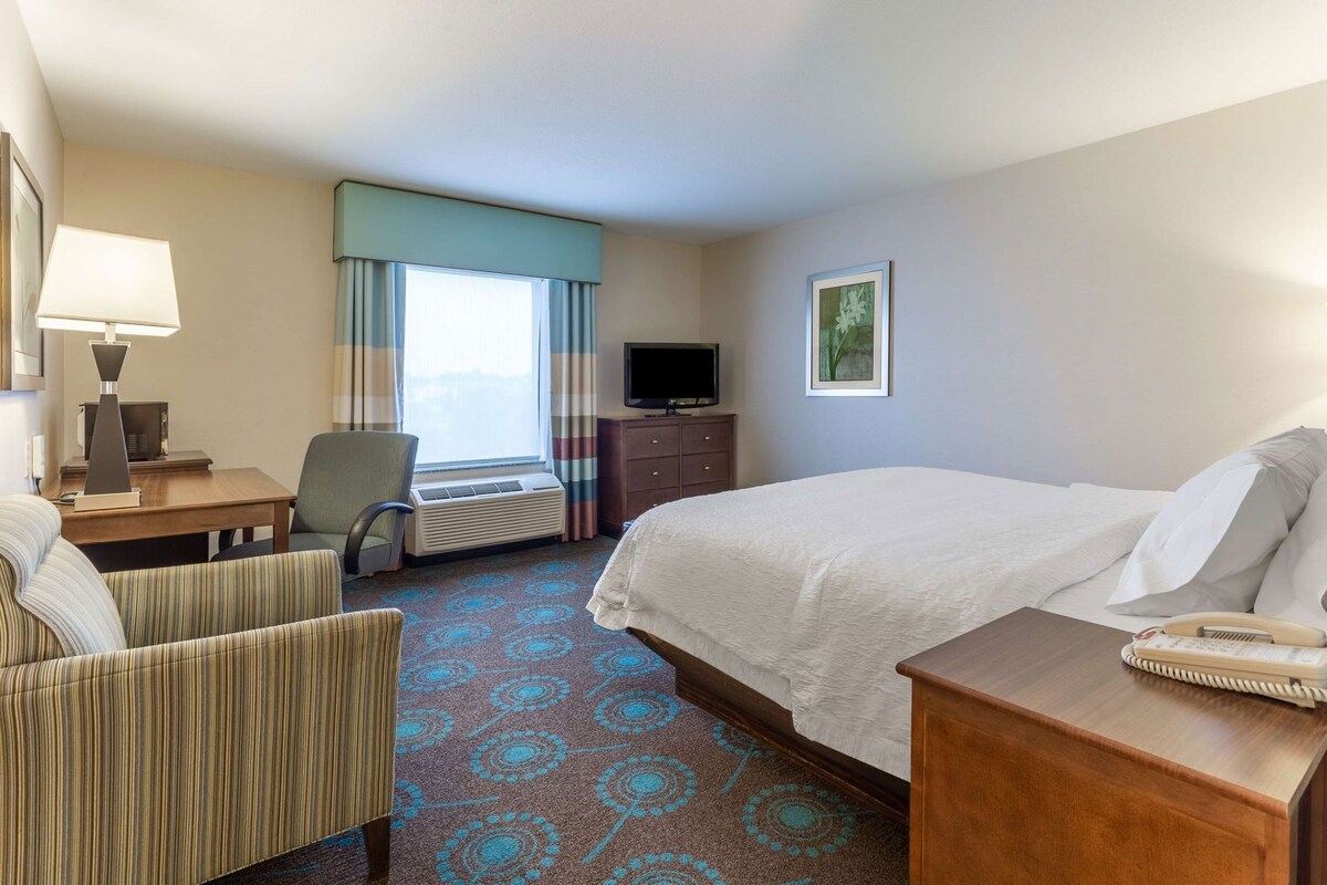 A hotel room with a bed, a desk, a chair, a television, and a window with curtains.