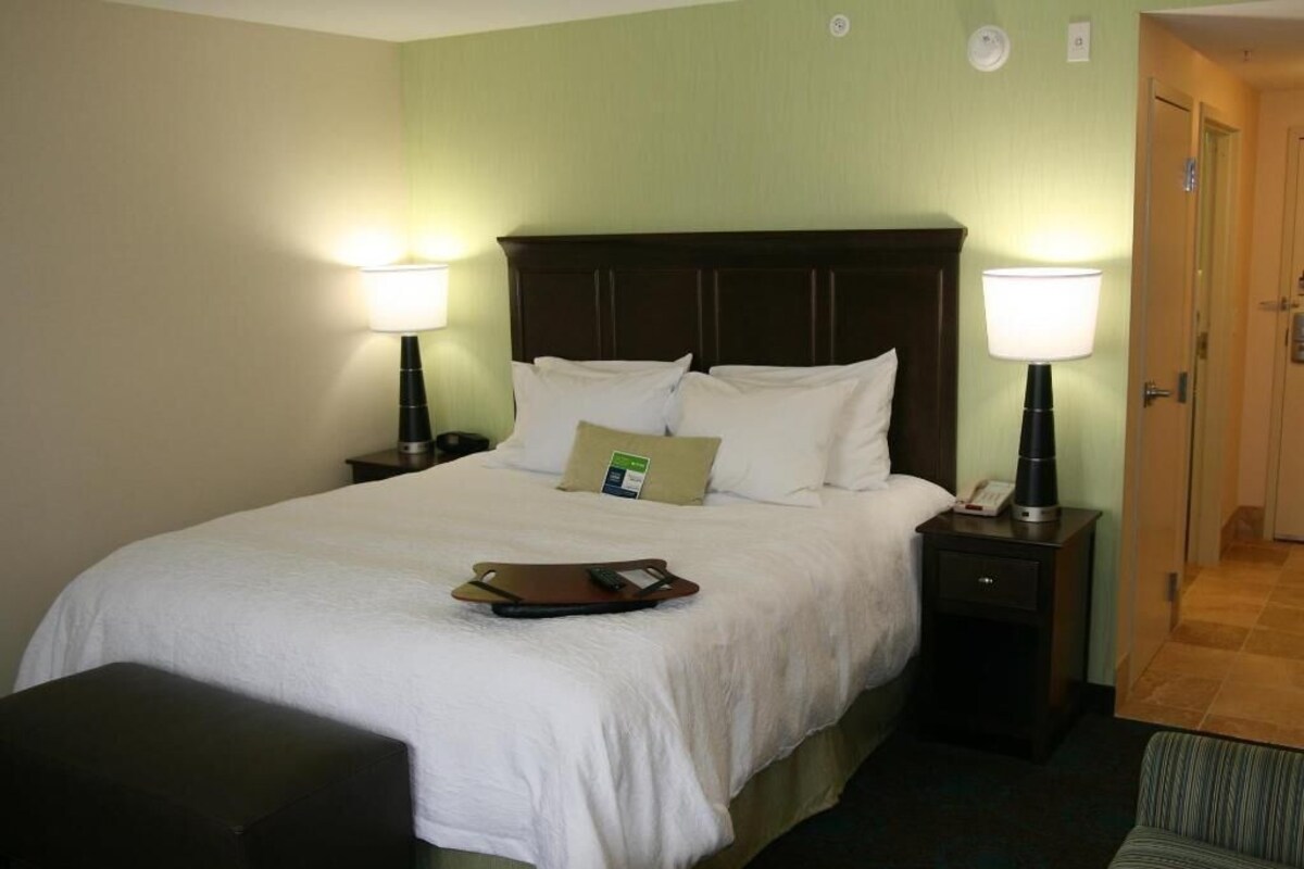 A hotel room with a bed, two bedside lamps, a nightstand, a small table, a chair, and a door.