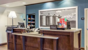 A hotel reception desk with a computer, phone, and a large poster of silos. - Hampton Inn Minneapolis/Shakopee (Shakopee)