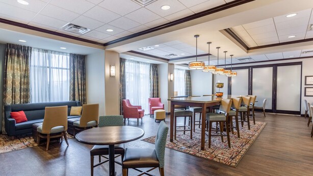 A hotel lobby with a round dining table, multiple chairs, a sofa, and a large window with curtains. - Hampton Inn Minneapolis/Shakopee (Shakopee)