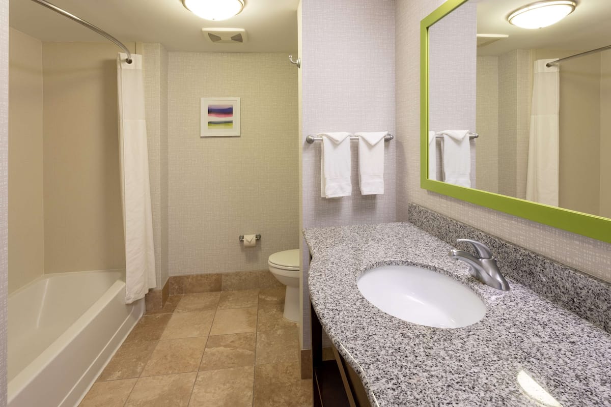 A bathroom with a bathtub, toilet, sink, and a mirror with a green frame.