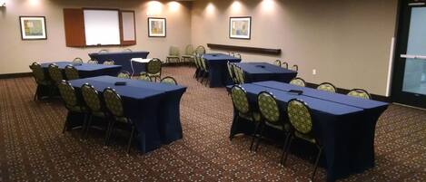Un salón de conferencias con varias mesas y sillas, piso alfombrado y cuadros en las paredes.