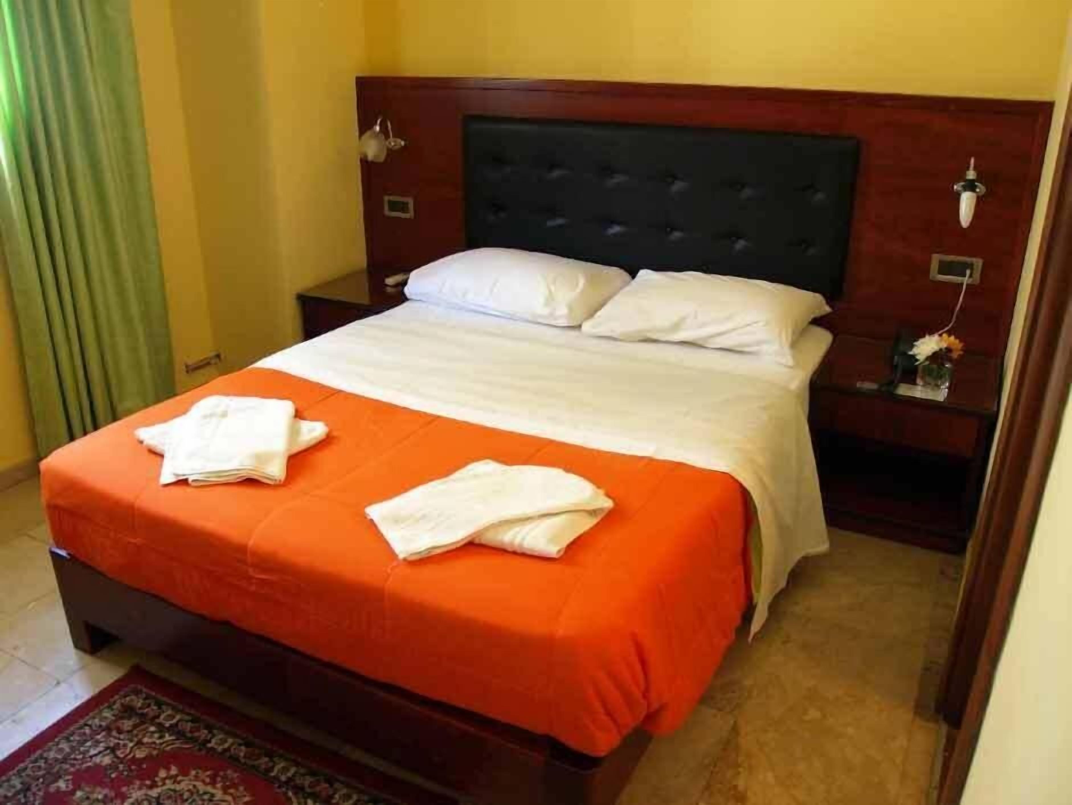 A hotel room with a bed, a nightstand, a lamp, and a window with curtains.