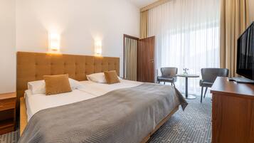 A hotel room with a large bed, a desk, a chair, and a television.
