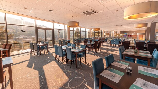 A spacious restaurant with high ceilings, large windows offering a city view, and modern furnishings. - Hotel Krynica Conference & SPA (Krynica-Zdroj)